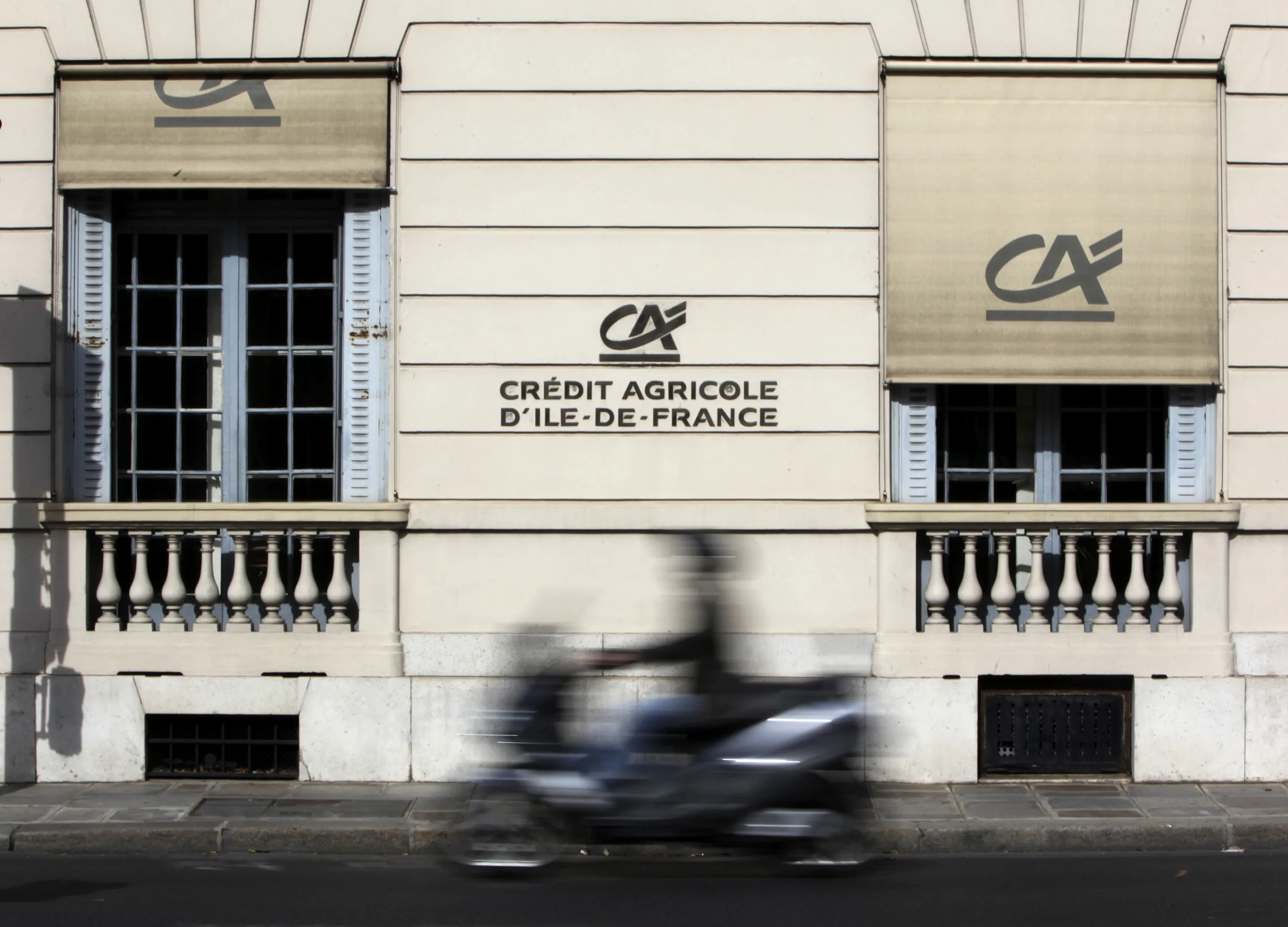 A motorcyclist passes a branch of Credit Agricole SA in Paris, France.