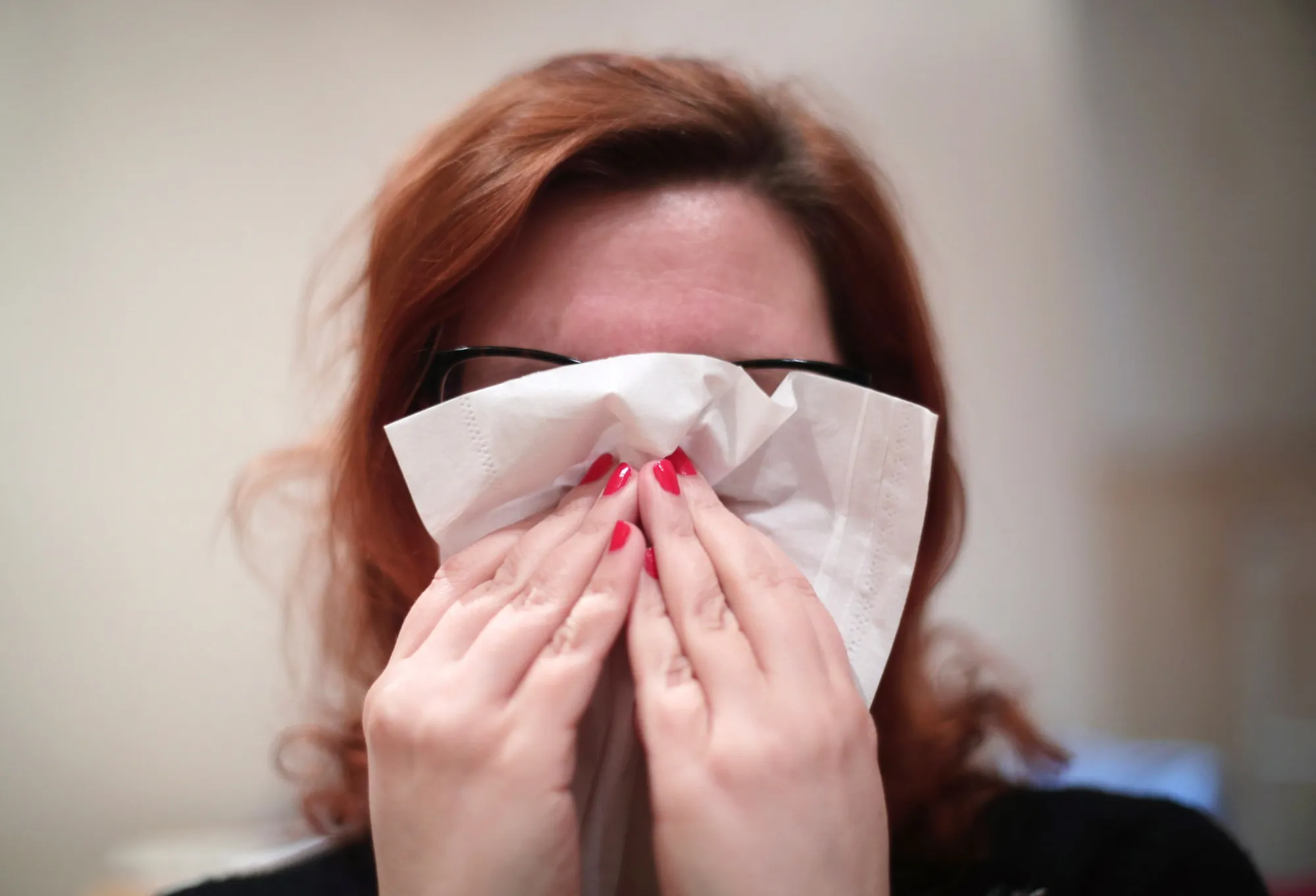 A woman&nbsp;blowing her nose with a tissue.