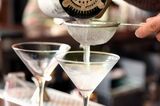 a bartender pouring martinis into chilled glasses through a small wire mesh strainer. RF