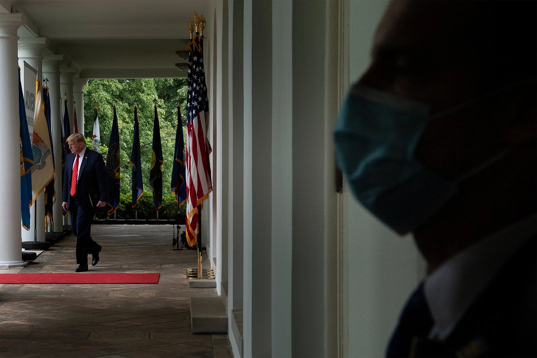 President Donald Trump arrives for a briefing on the U.S. response to coronavirus. The Secret Service member, right, is wearing a face mask.