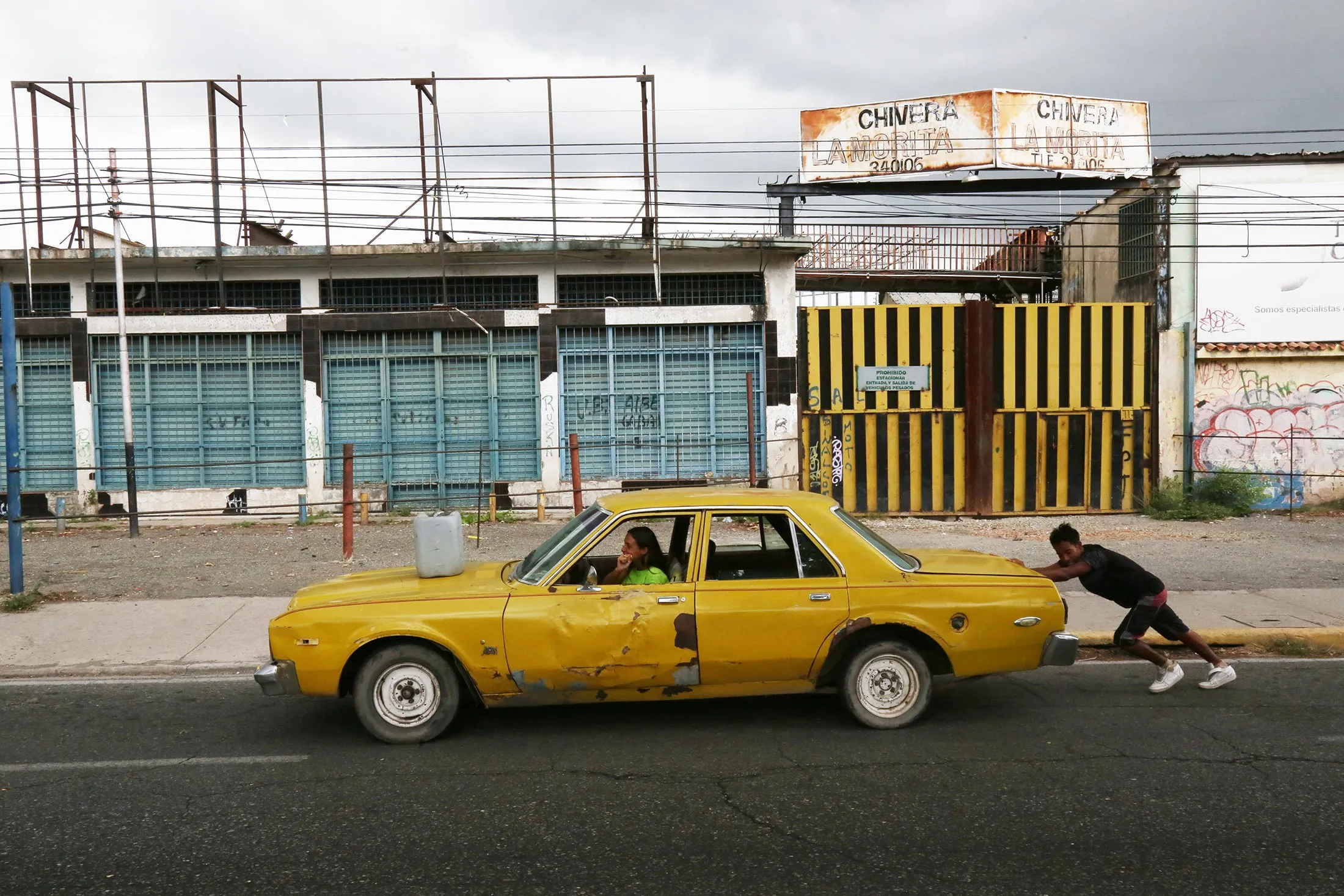 A young man pushes a car while a woman takes the steering wheel on their way to a gas station where they expect to fill the tank during a fuel shortage in Maracay, Venezuela.&nbsp;