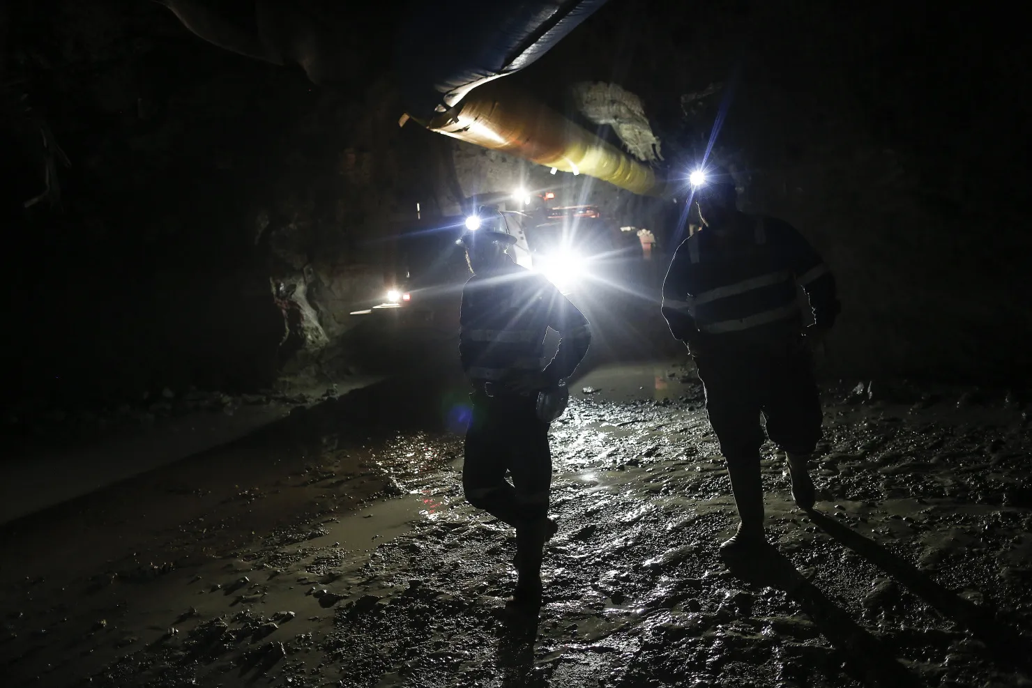 Mine workers inspect a rock wall by flashlight while identifying drilling locations in the underground tunnels at the Kibali gold mine.
