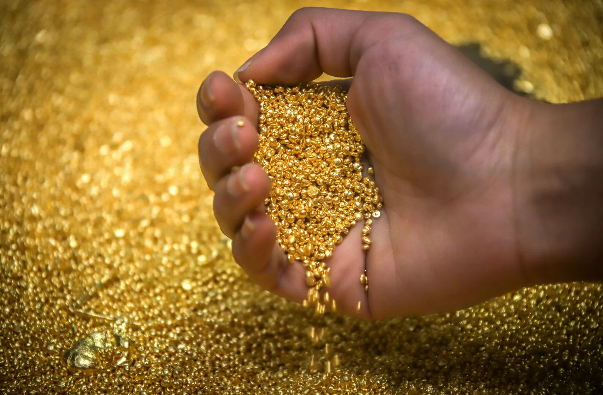 A worker checks gold granules at a refinery smelter.