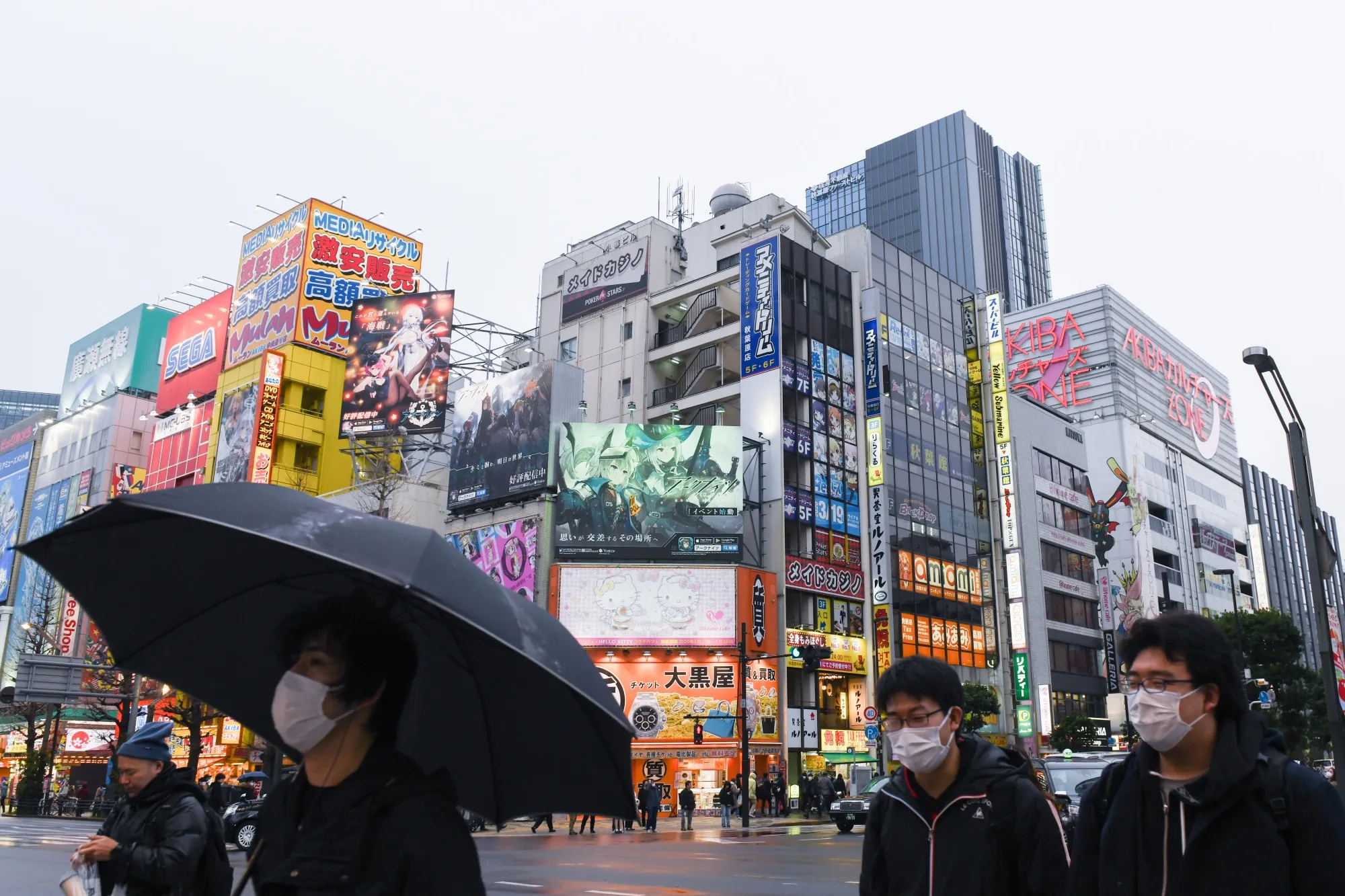 Pedestrians wearing protective masks walk past stores in the Akihabara shopping district of Tokyo.