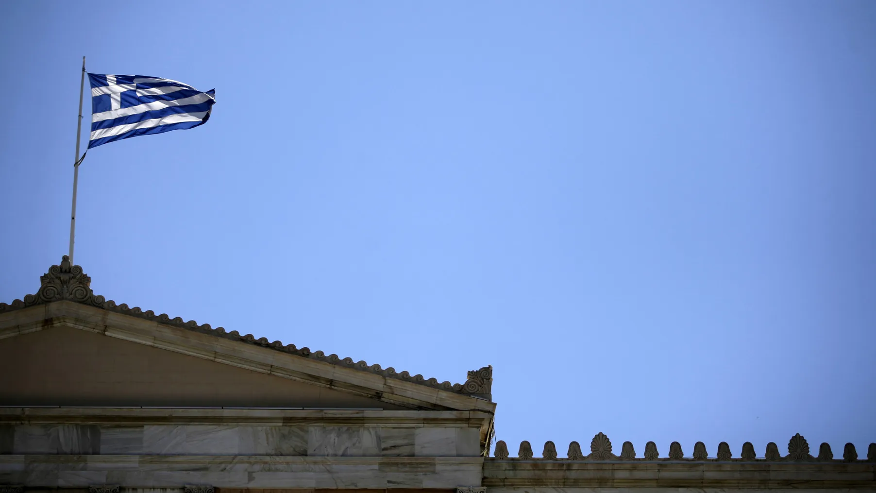 The Greek national flag flies atop a building near Syntagma Square in Athens, Greece

