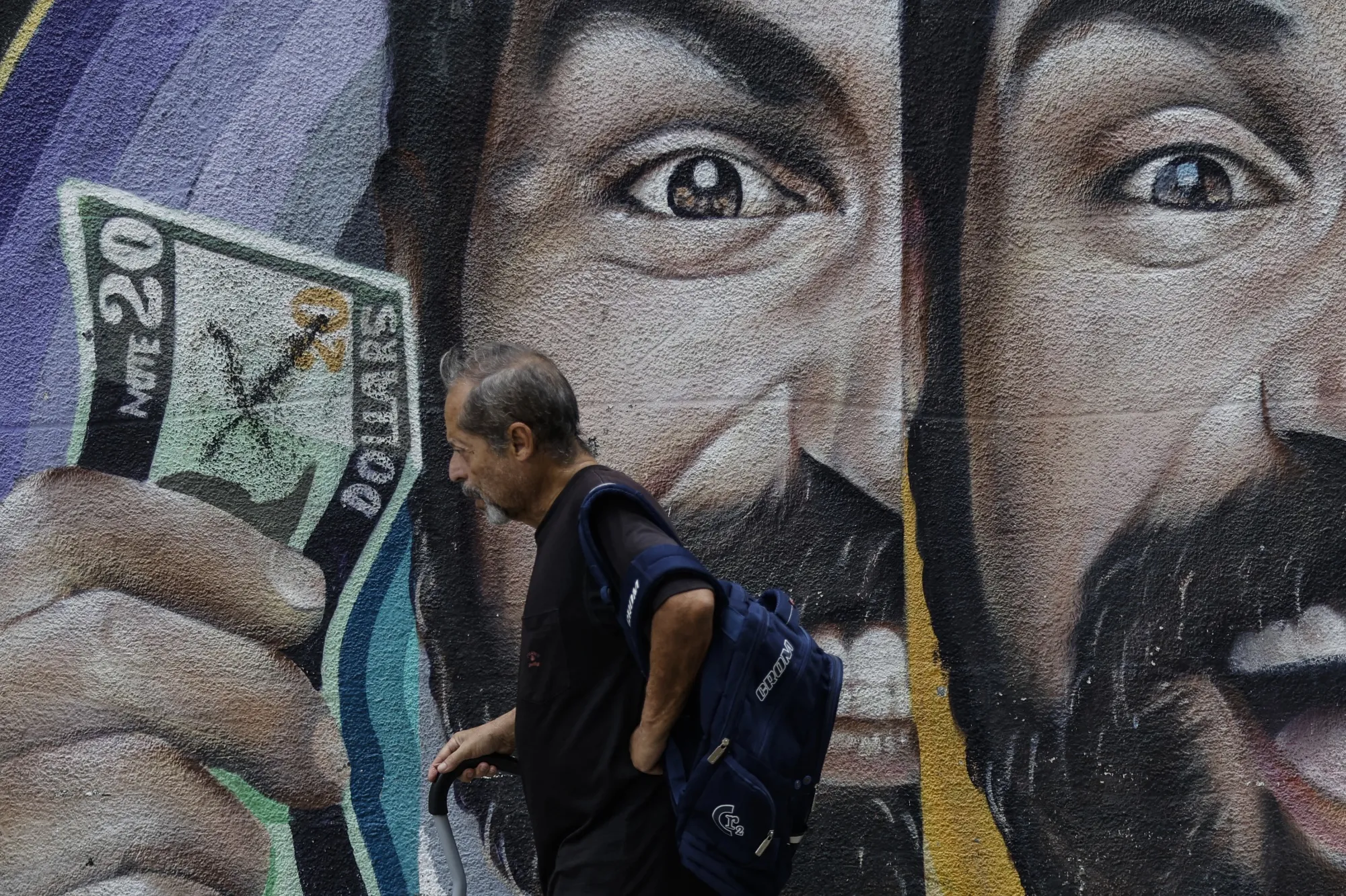 A man passes a foreign-exchange themed mural in Caracas on June 2. The widening gap between the official and black-market rates threatens to fuel inflation.