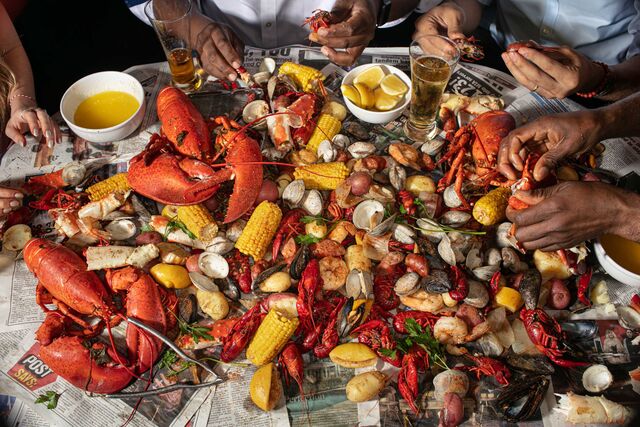 Seafood boil on large table wrapped in newspaper. Seafood contents include lobster, crab mussels, clams, potatoes, corn, and melted butter.