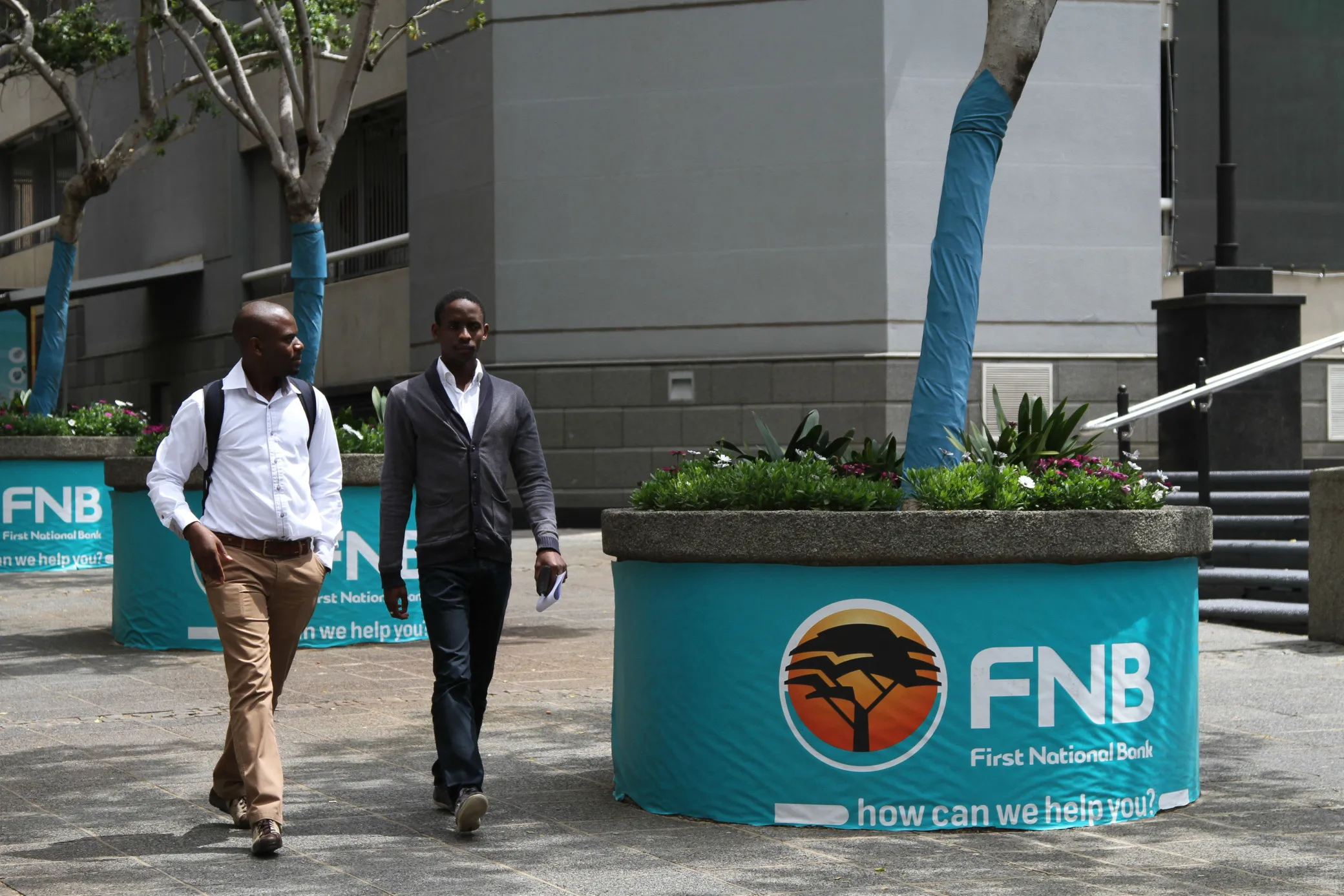 Pedestrians pass street advertising for First National Bank (FNB), a division of FirstRand Bank Ltd., in Johannesburg.