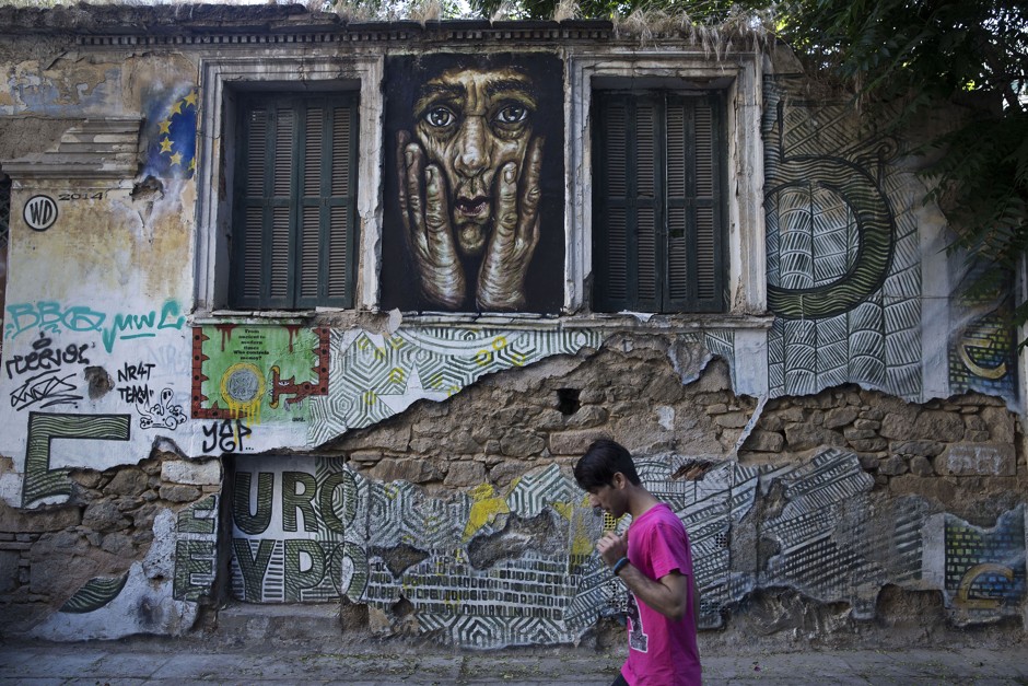 A man walks by an abandoned Athens house covered in street art by WD (Wild Drawing) and Ore.