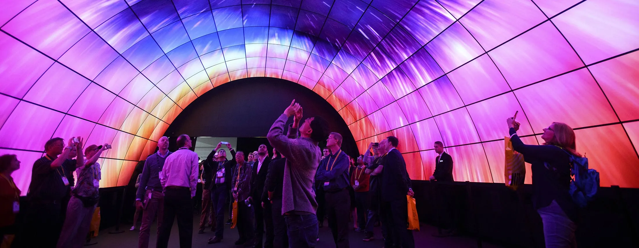 Attendees take photographs with mobile devices while standing under a tunnel wall of LG OLED 4K TVs during the 2017 Consumer Electronics Show (CES) in Las Vegas, Nevada, U.S., on Thursday, Jan. 5, 2017. CES, celebrating its 50th year, will showcase self-driving cars, TVs, drones, robots and a slew of other gadgets.
