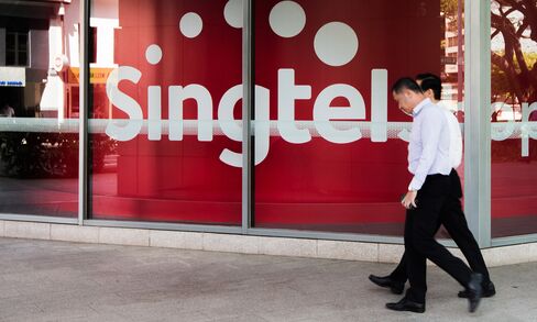 Pedestrians walk past a Singtel logo in Singapore.