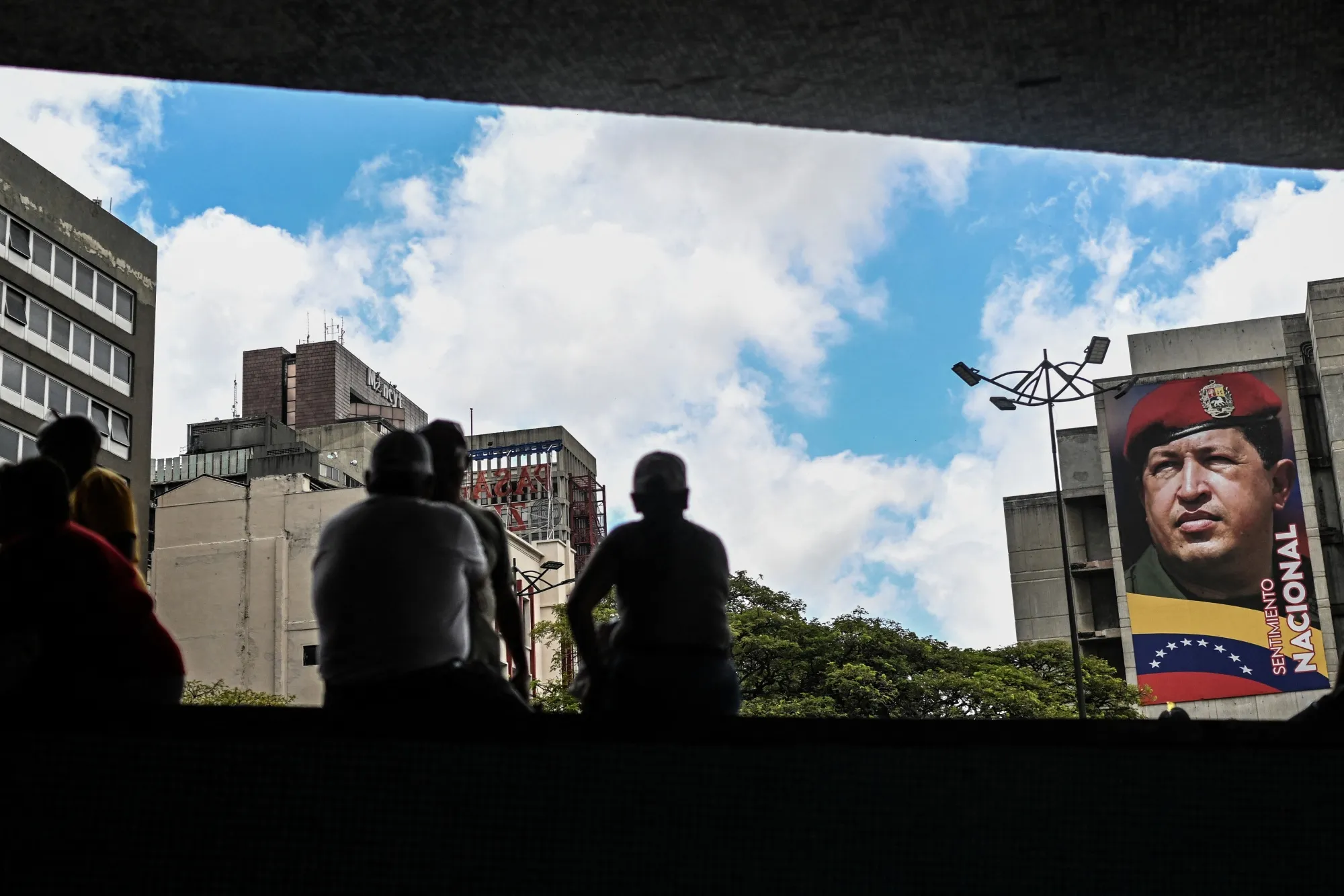 People sit in front of a mural of Venezuela's former President Hugo Chavez in Caracas.