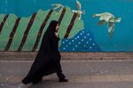 A woman wearing a chador walks past a wall mural on a street in Tehran.
