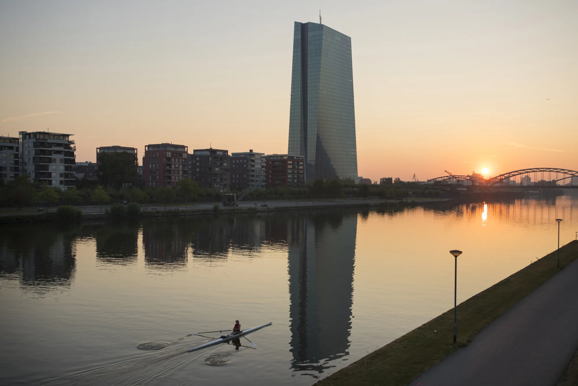A rower paddles on the River Main as the skyscraper headquarters of the European Central Bank&nbsp;stands beyond as the sun rises in Frankfurt.