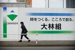 A pedestrian walks past the Obayashi Corp. logo displayed on a fence at a construction site in Tokyo, Japan.