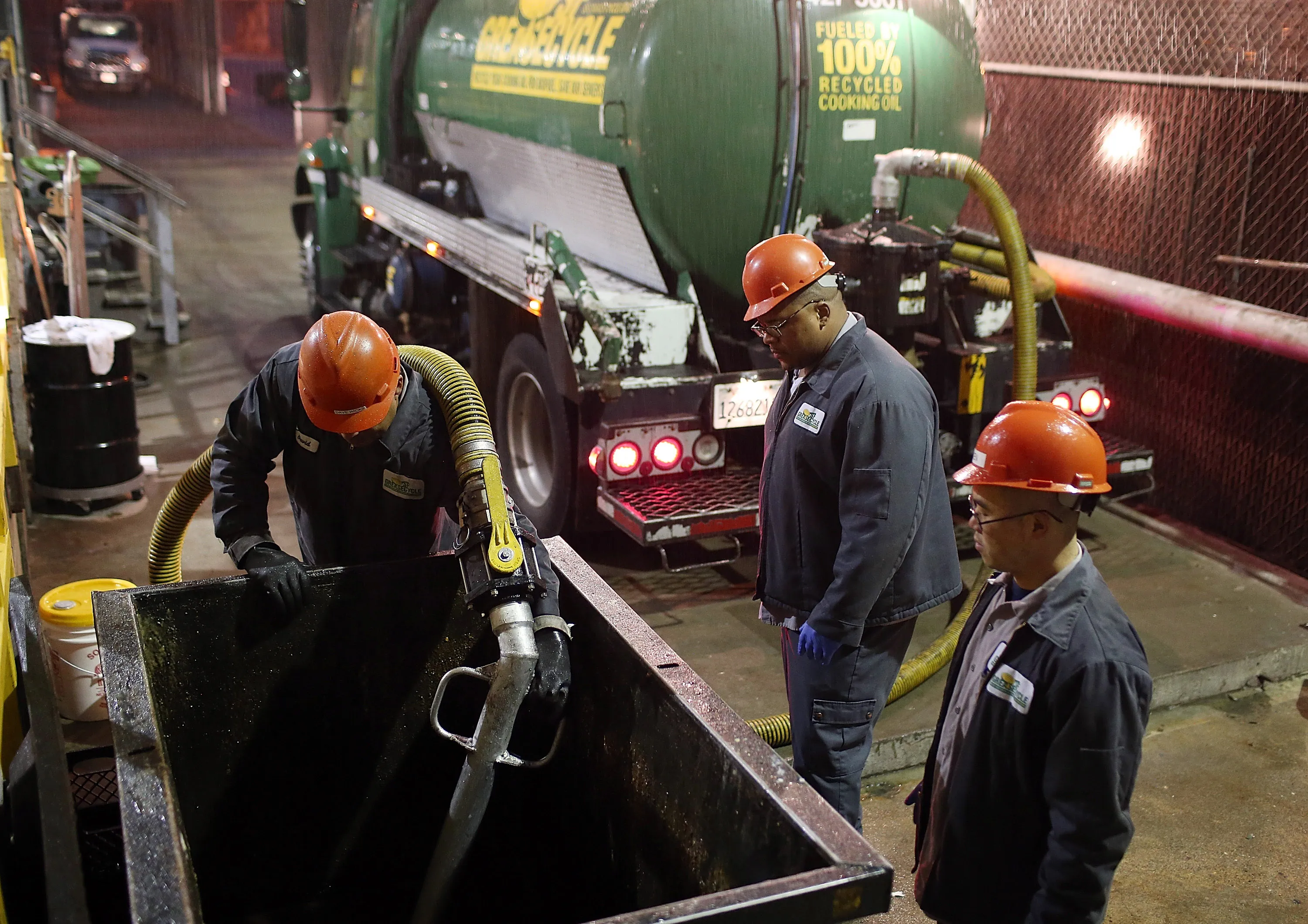 Workers use&nbsp;a hose to transfer oil from a dumpster into a grease collection truck in San Francisco, California.
