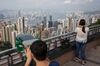 A tourist, left, uses binoculars to look at the view from Victoria Peak as commercial and residential buildings stand in the distance in Hong Kong, China, on Tuesday, April 28, 2015. Total visitors to Hong Kong, including those from China, fell 12.4 percent during the April 3 to 7 Ching Ming and Easter holidays, the government said, with Chief Executive Leung Chun-ying describing the decline as a "wake up call" and listing anti-parallel trading protests among reasons for the drop.