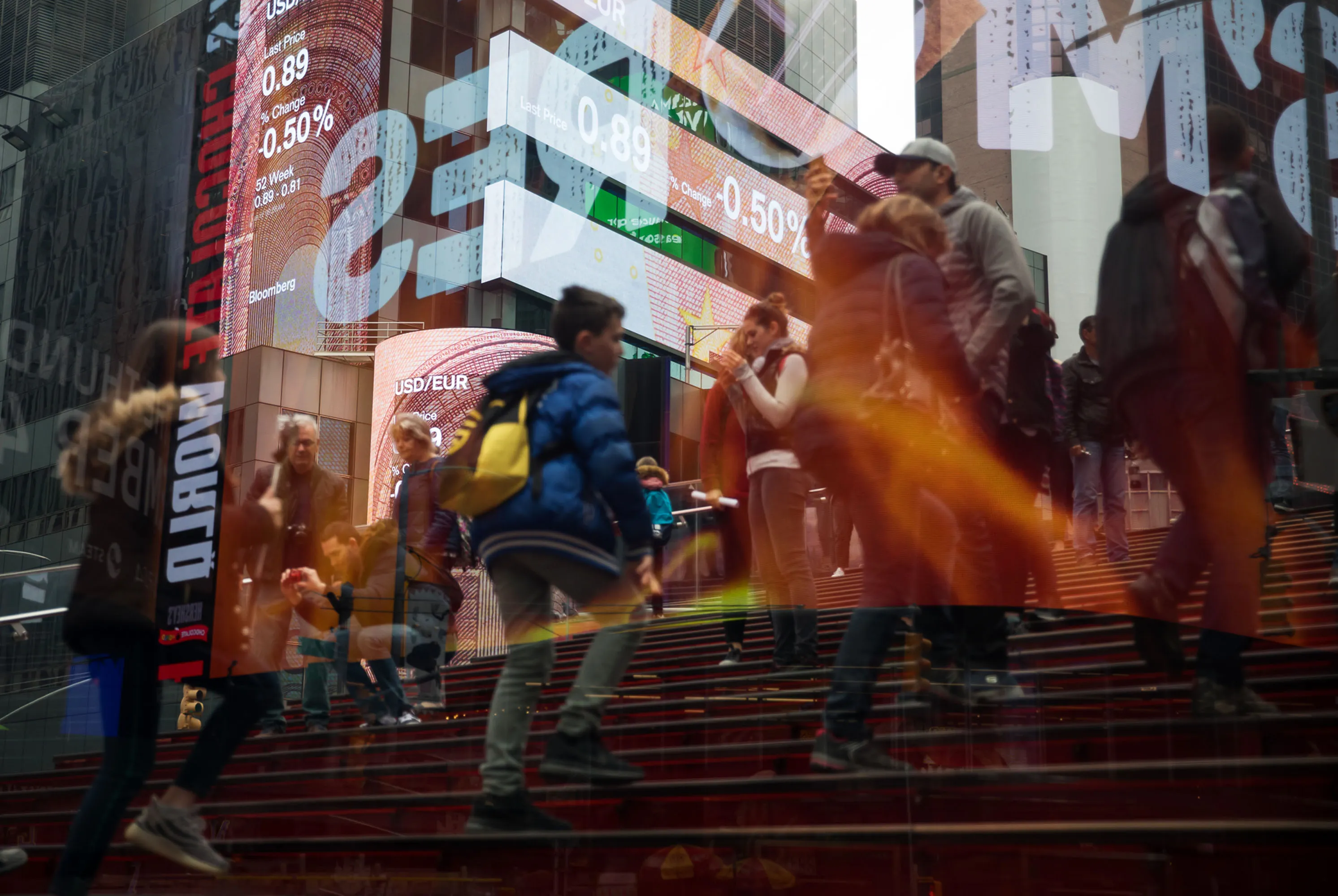 Pedestrians stand in front of monitors displaying the U.S. Dollar and Euro&nbsp;exchange rates.