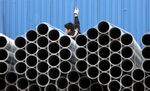 A worker stands behind stacked steel pipes at a storage yard in Shanghai, China,
