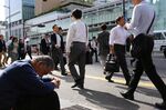 Morning commuters walk past a man sitting outside Shinjuku Station in Tokyo.