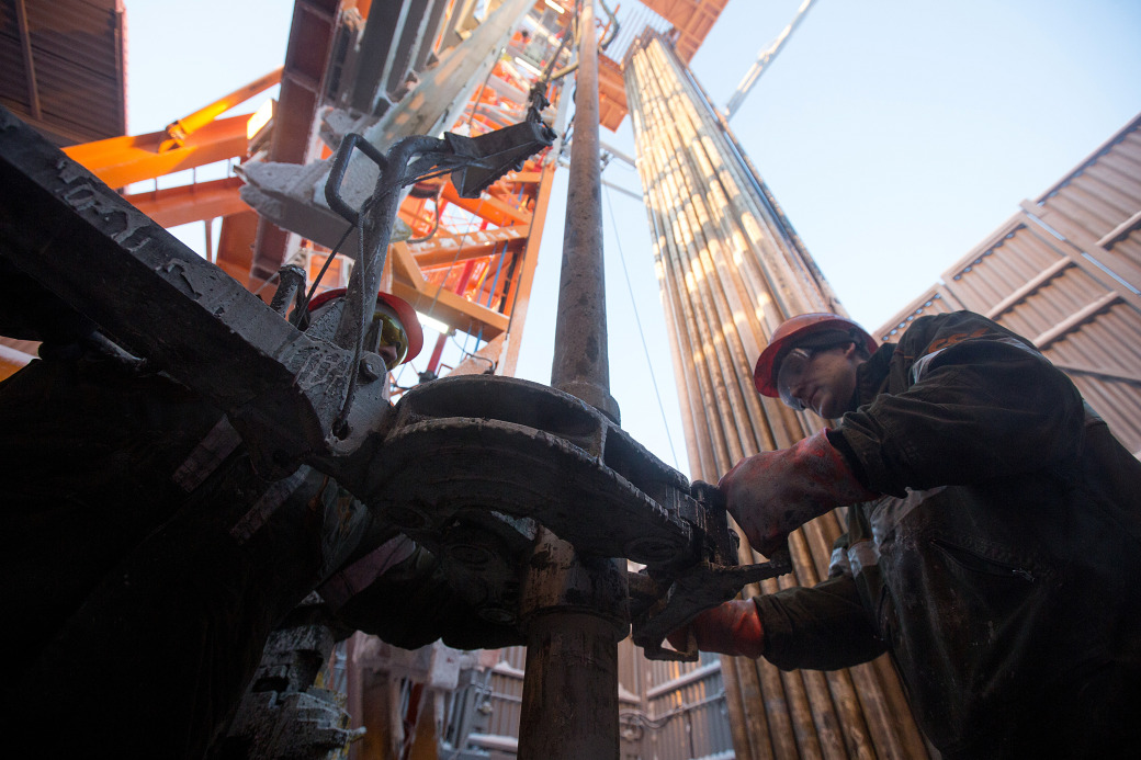 Workers use machinery to move drill sections on the drilling floor of the oil derrick in the Salym Petroleum Development oil fields in Salym, Russia.