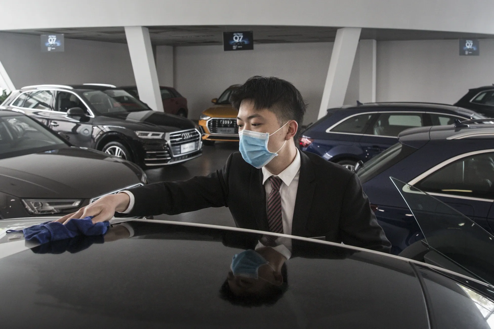 An employee wearing a protective mask wipes a vehicle on display inside an Audi AG dealership in Wuhan.