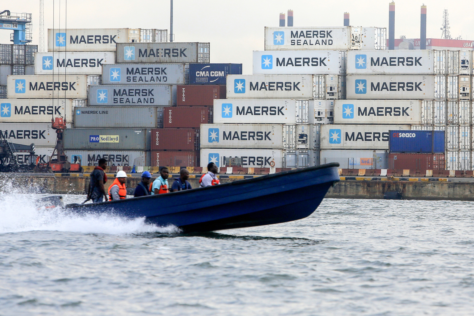 People ride on a boat past A.P. Moeller-Maersk branded shipping containers&nbsp;in Lagos.