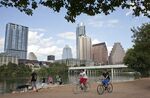 Cyclists pass beneath the downtown skyline on the hike-and-bike trail on Lady Bird Lake in Austin.