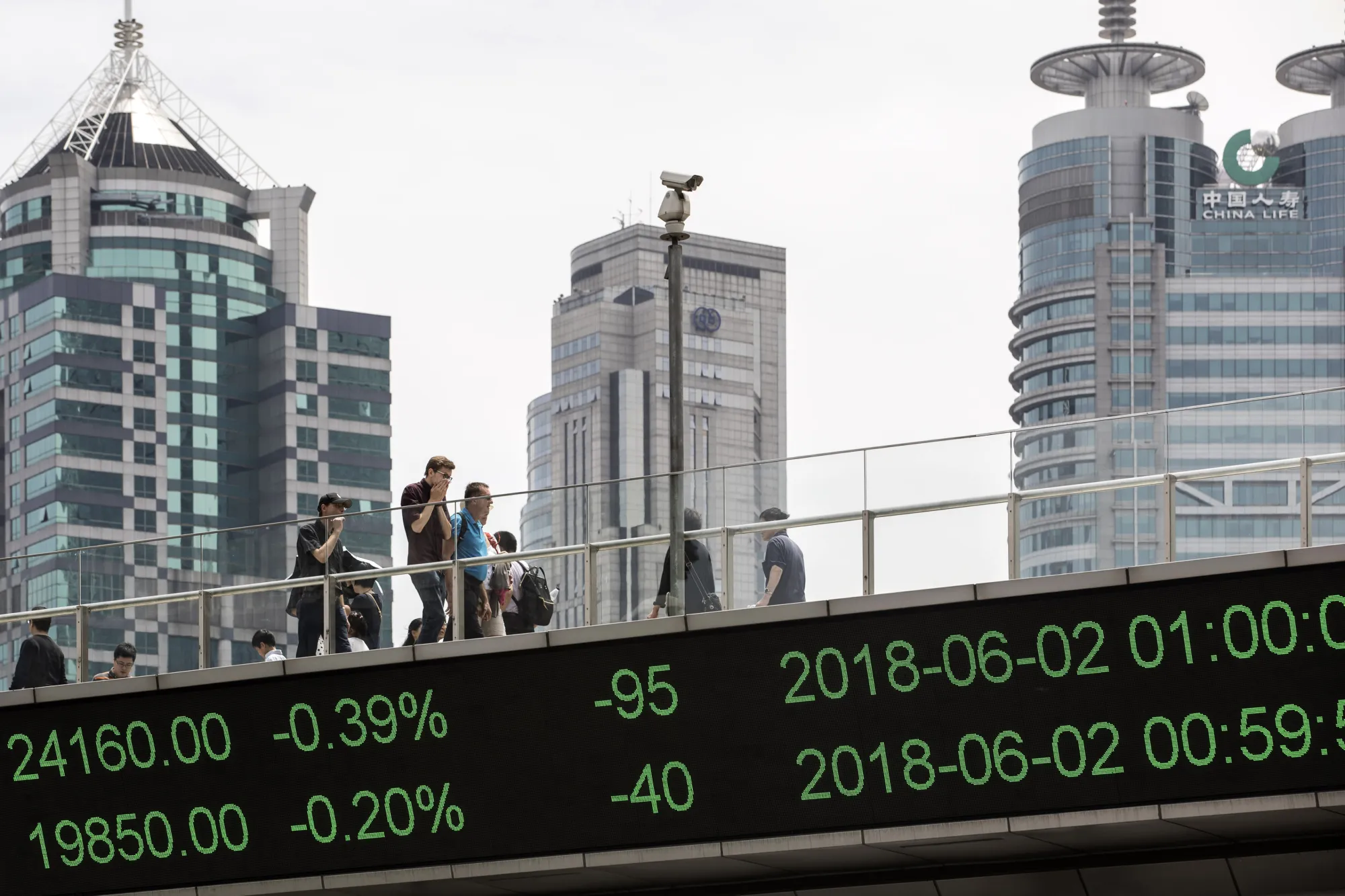 People walk along an elevated walkway as an electronic ticker displays stock figures in Shanghai,.