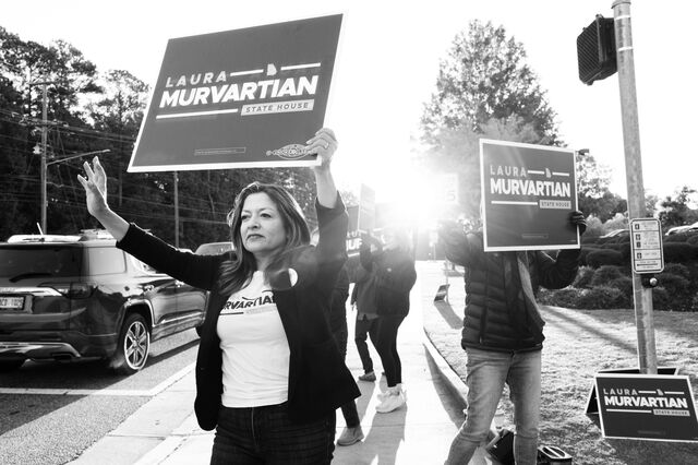  Murvartian and volunteers hold campaign signs on the side of the road as cars travel past them.