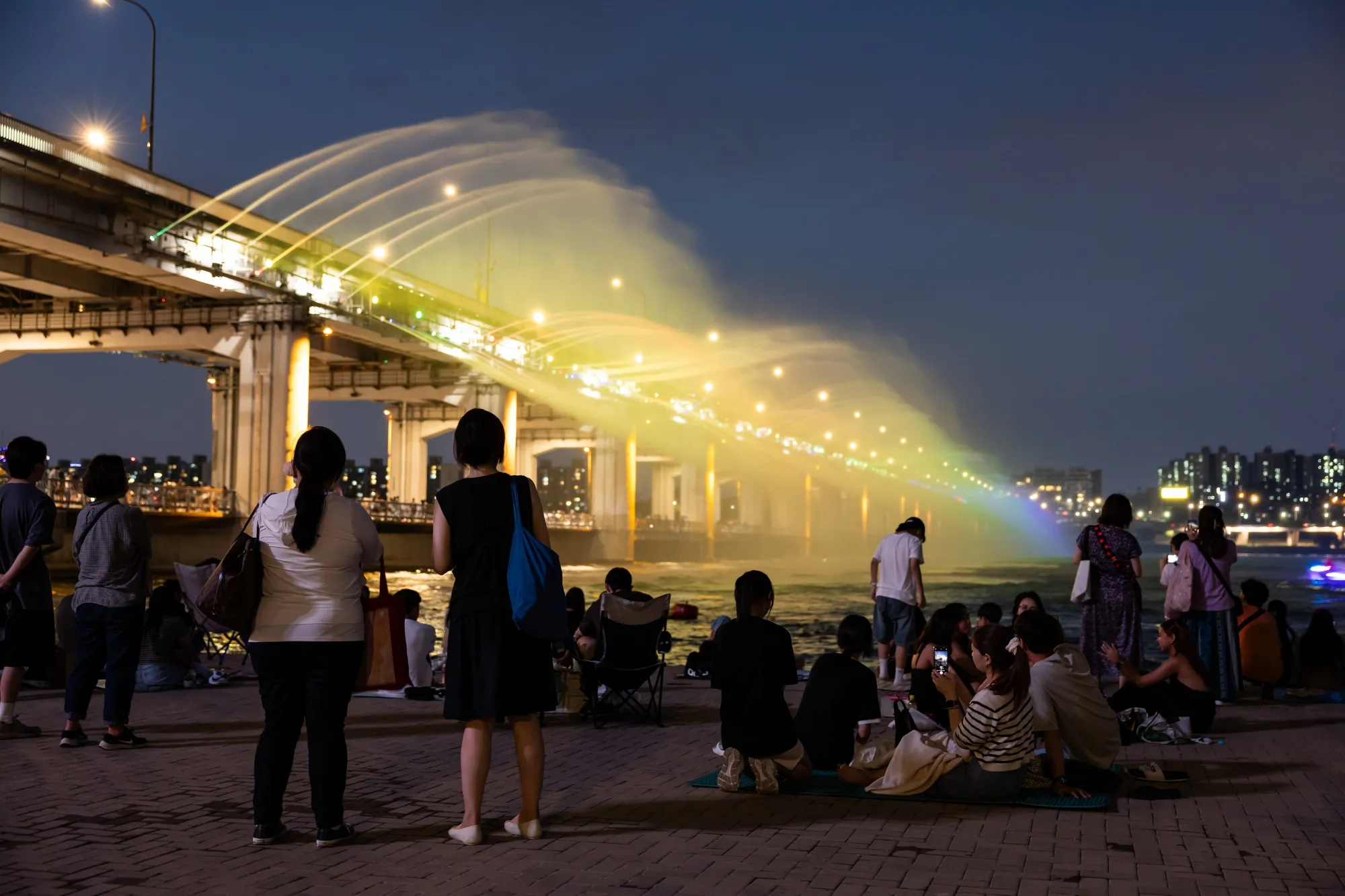 People look at water being sprayed from a fountain on Banpo Rainbow Bridge at night in Seoul, South Korea, on Sunday, Aug. 4, 2024. The Korea Meteorological Administration issued a heat wave warning across the country on Aug. 6.