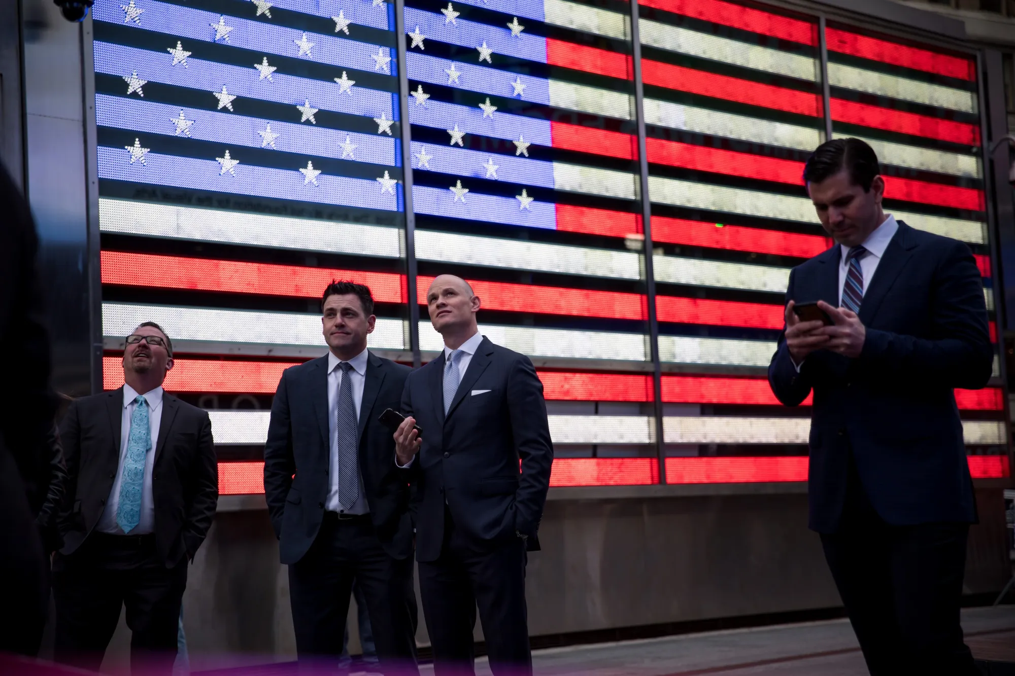 Pedestrians stand in front of an illuminated American flag in the Times Square neighborhood of New York.