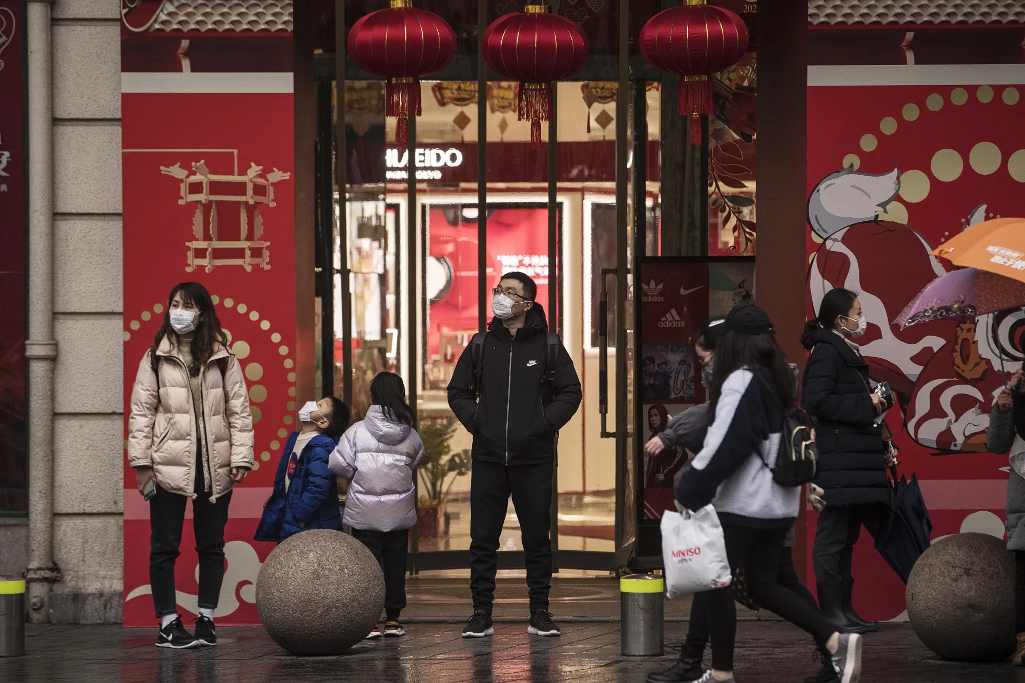 Pedestrians wearing protective masks stand in front of a department store ahead of the Lunar New Year in Shanghai on Jan. 23.