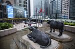 Sculptures of water buffaloes stand as pedestrians walk past an electronic ticker board and screens displaying stock figures outside the Exchange Square complex, which houses the Hong Kong Stock Exchange.