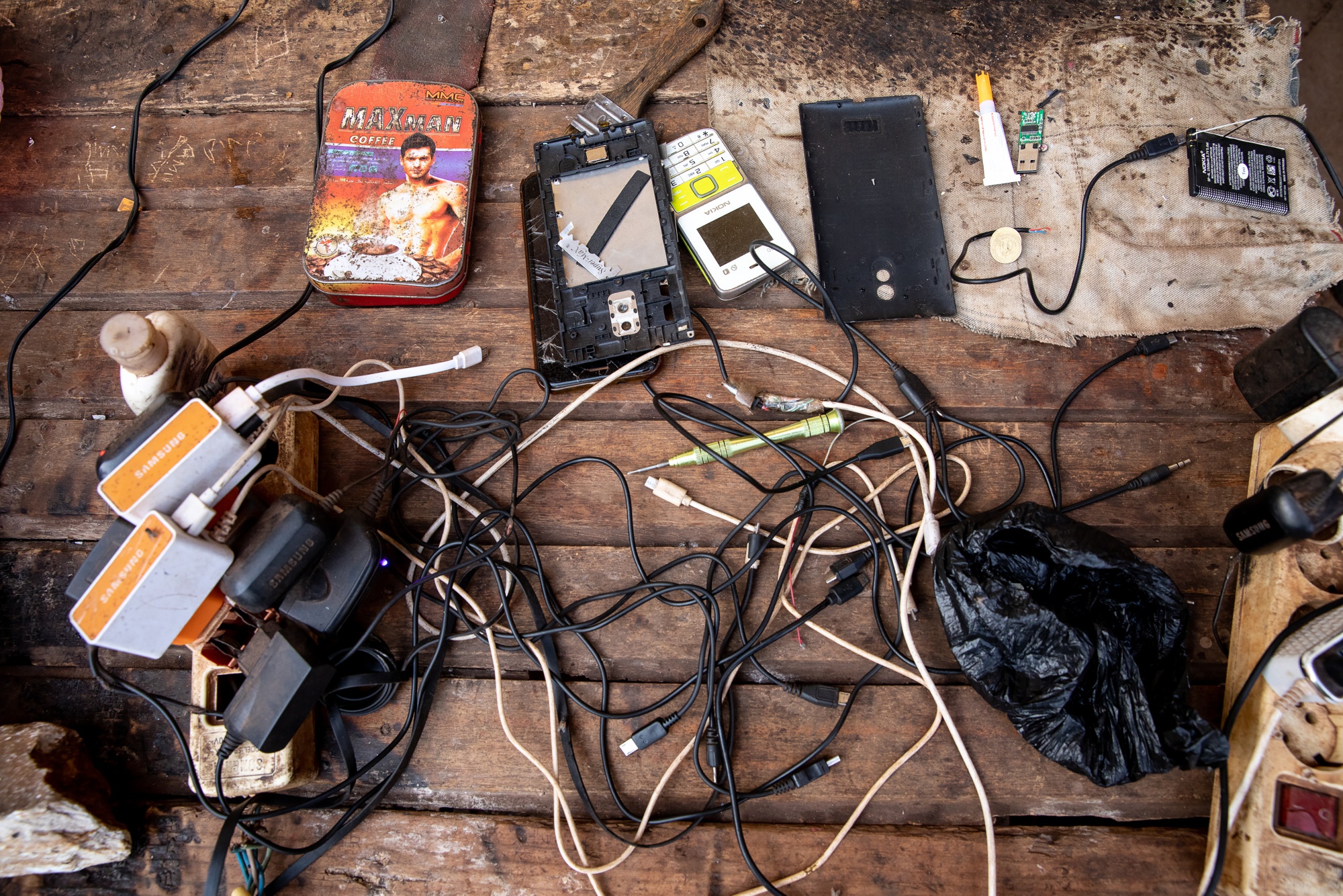 Charging cables, a disassembled mobile phone and tools sit on a work bench at a phone repair kiosk in Bangui Central African Republic, on Friday, March 15, 2019.&nbsp;