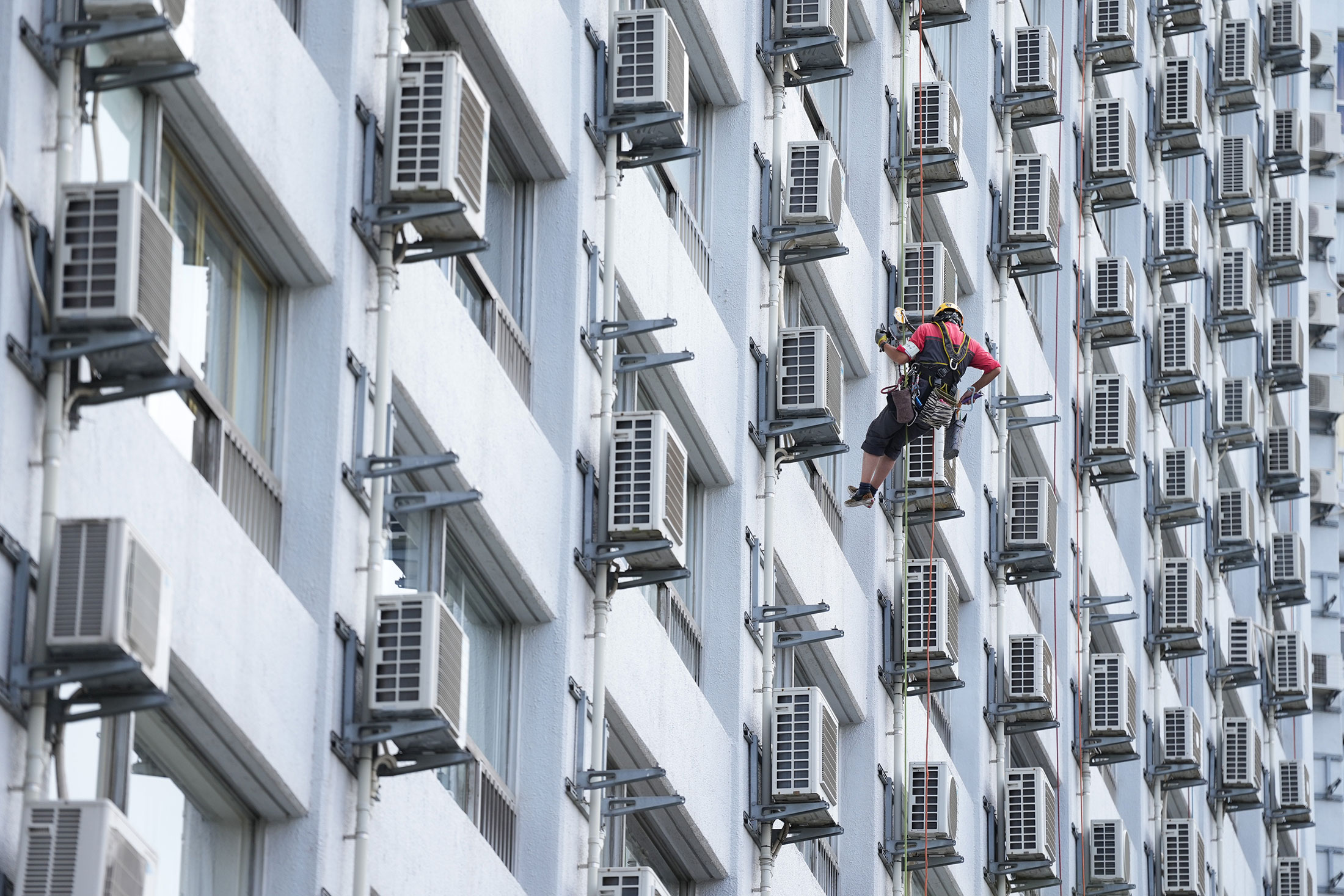 A worker washes windows next to air conditioning units at an apartment building in Tokyo, Japan, on Friday, July 21, 2023. 