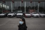 An employee wearing a protective mask stands in front of a row of vehicles on display at an Audi AG dealership in Wuhan.