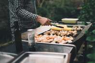 Holding tongs grilling prawns, meat and vegetables on barbecue