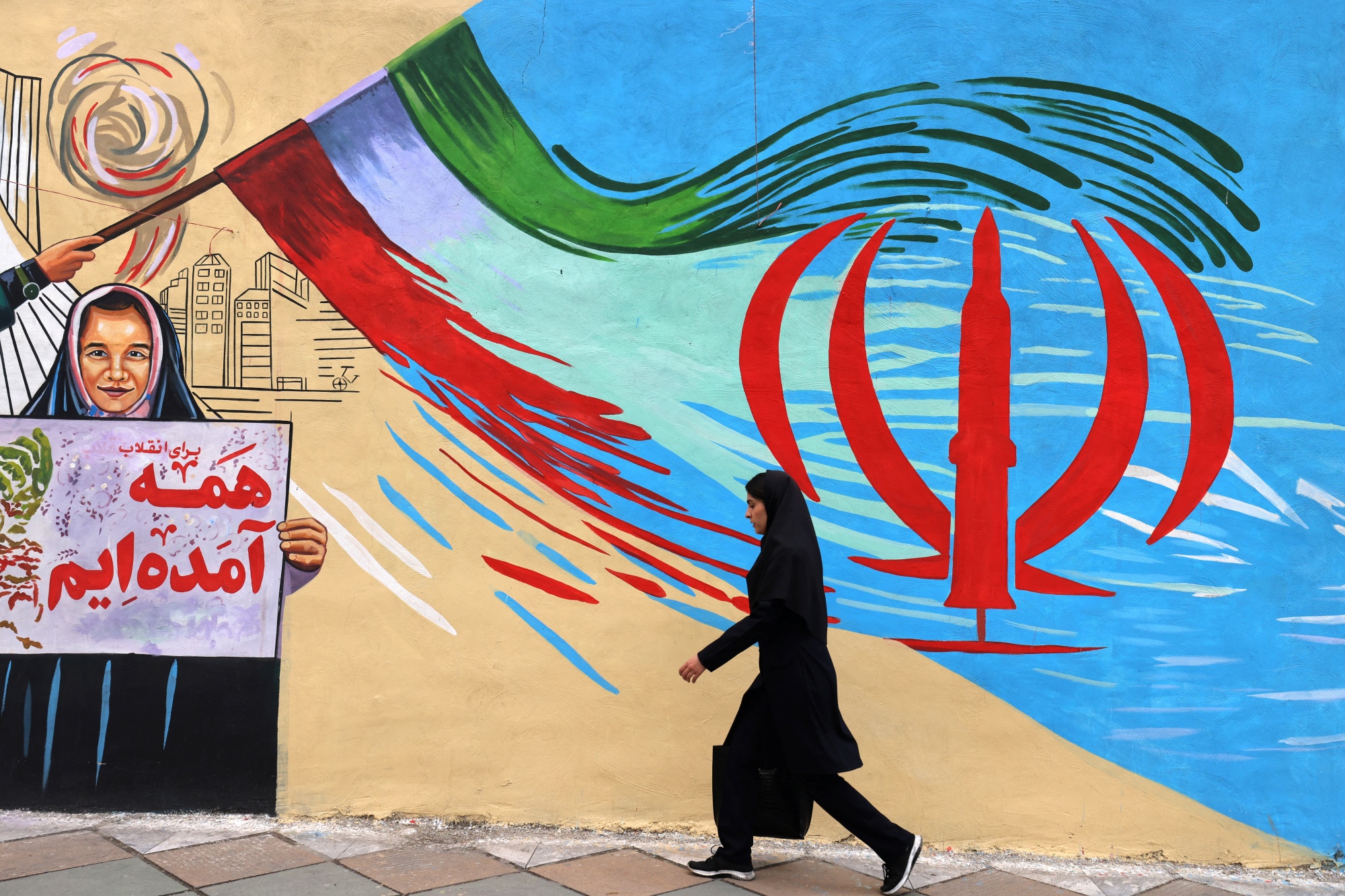TOPSHOT - An Iranian woman walks past an anti-USA and anti-Israel mural, in Tehran on April 21 2026, amid a ceasefire in the region. With the end of a two-week ceasefire approaching, the White House said US Vice President was ready to return to Pakistan for fresh negotiations to end a conflict that has sent crude soaring and revived inflation fears. (Photo by ATTA KENARE / AFP via Getty Images) / Photographer: ATTA KENARE/AFP