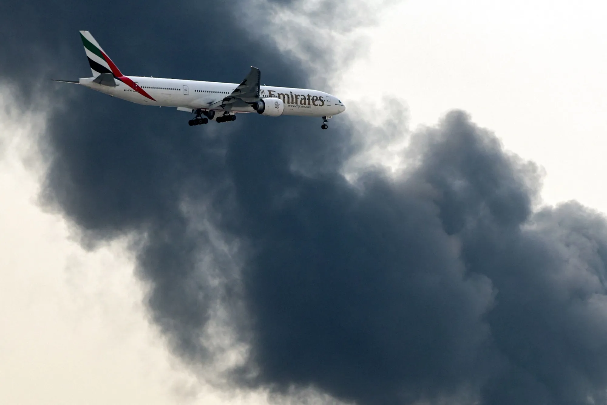 An Emirates aircraft prepares for landing as a smoke plume rises from an ongoing fire near Dubai International Airport on March 16.