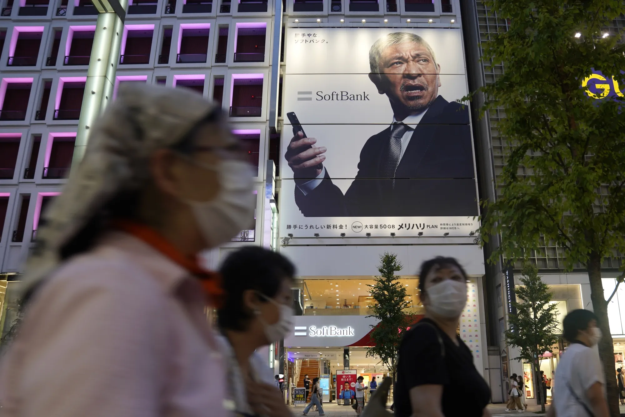 Pedestrians wearing protective masks walk past a SoftBank Corp. store in Tokyo.
