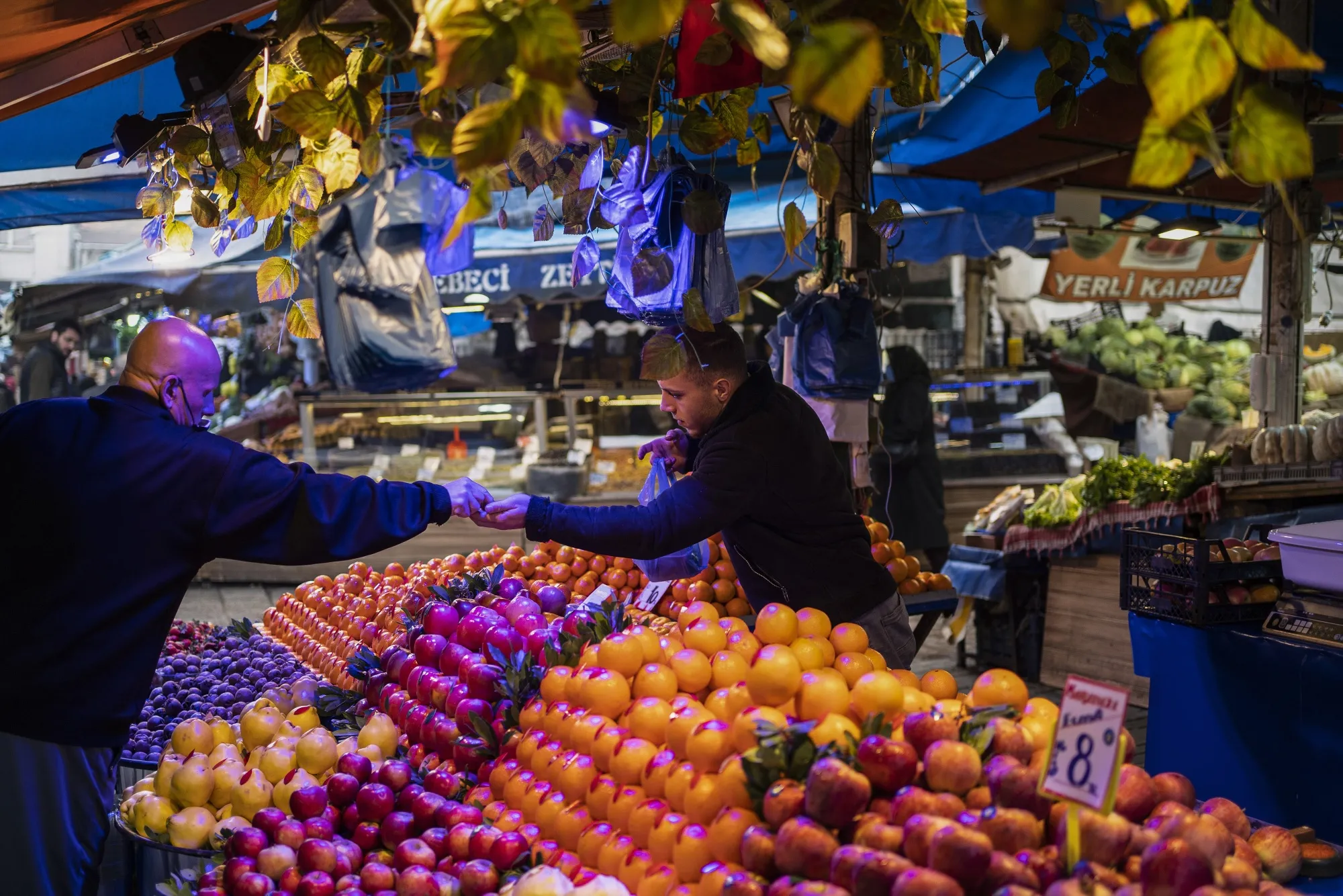 A vendor serves a customer at a fresh produce stall at a local market in Bursa, Turkey.