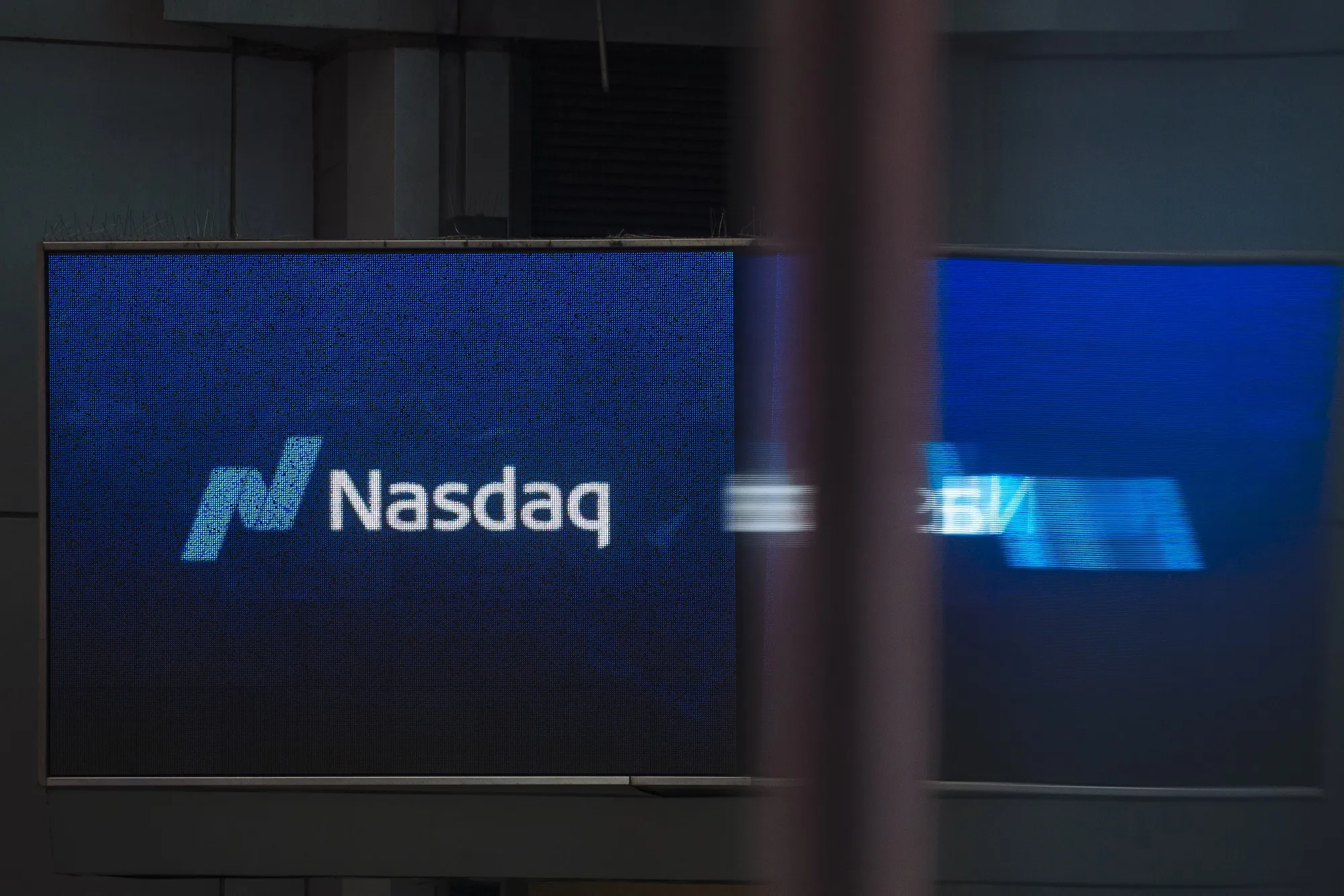 A screen displays the Nasdaq Inc. logo in Times Square.
