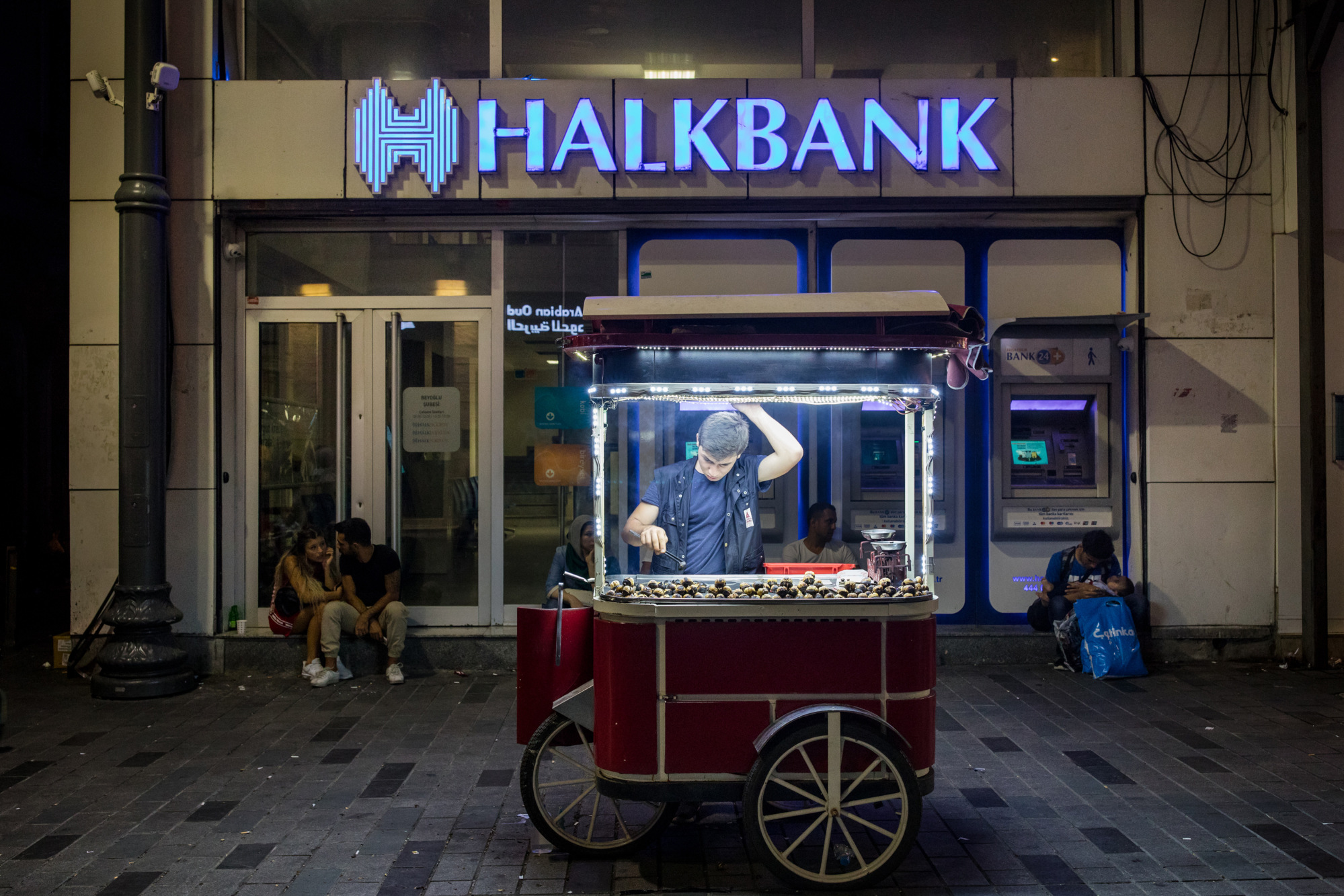 A chestnut seller waits for customers outside a branch of Turkiye Halk Bankasi AS, also known as Halkbank, in Istanbul.