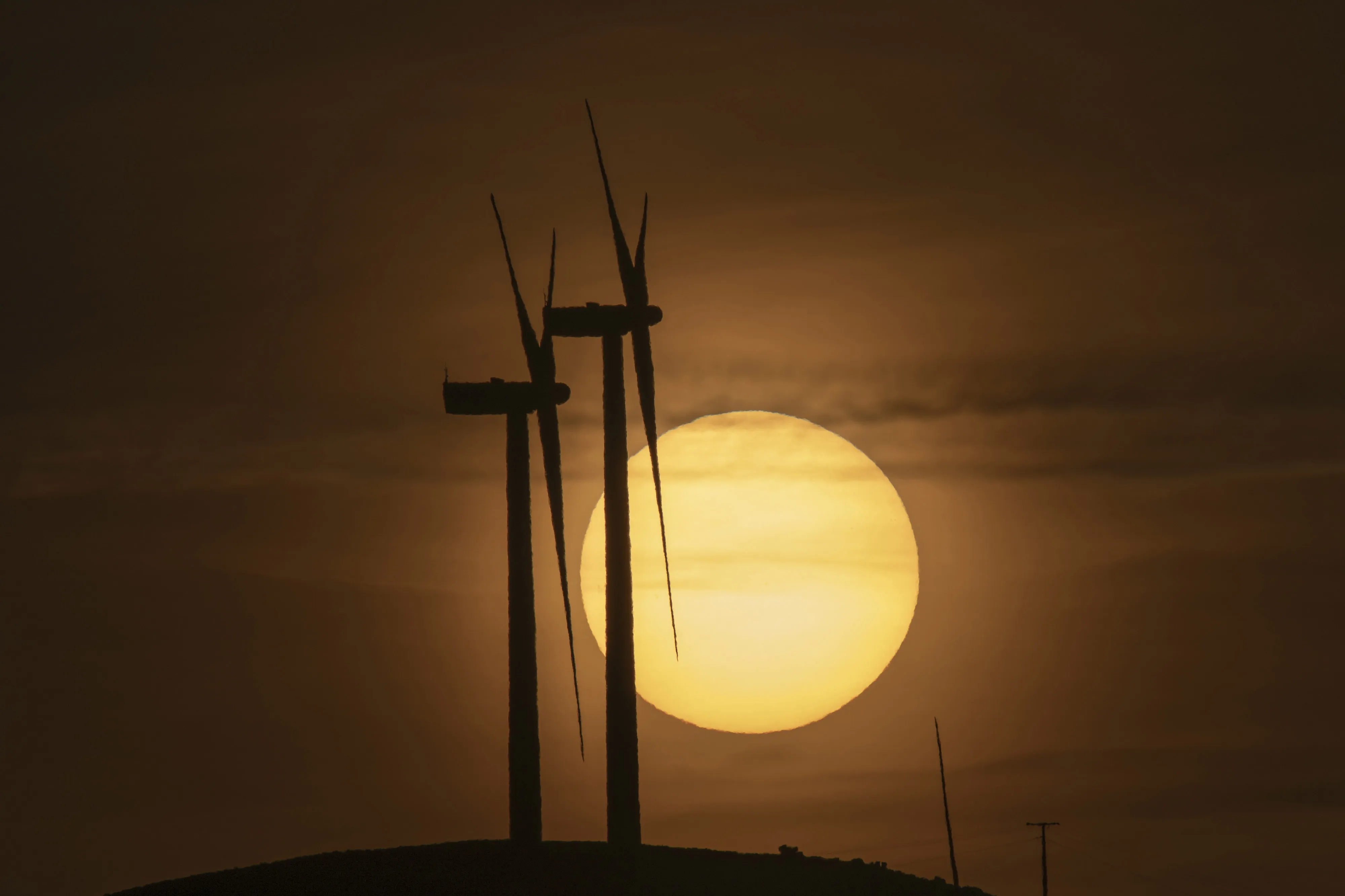 The sun rises beyond wind turbines at a wind farm in Muras, Spain.