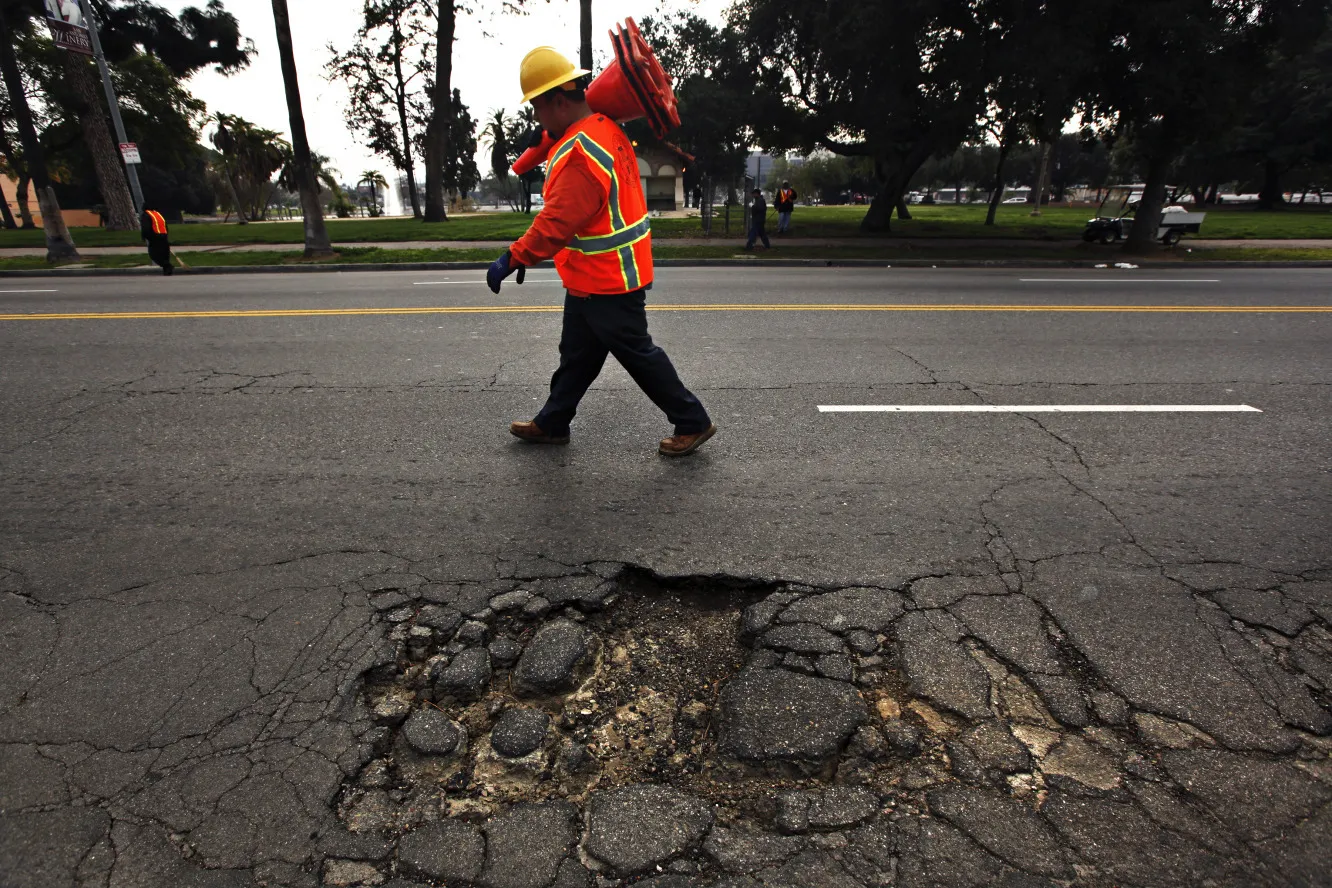 A road worker walks by a large pothole on N. Mission Rd. near Lincoln Park Ave. in Los Angeles. Photographer: Liz O. Baylen/Los Angeles Times/Getty Images
