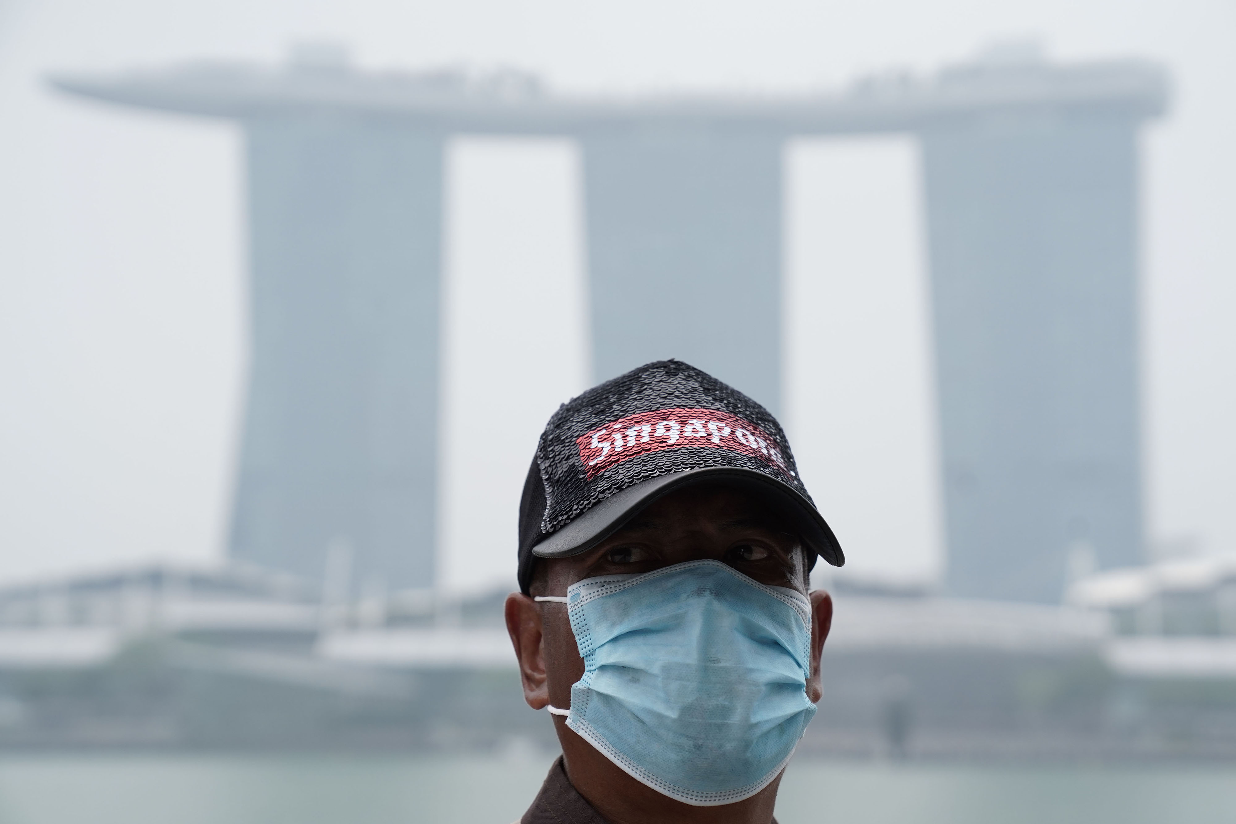 A man wears a face mask in front of the haze shrouded Marina Bay Sands hotel and casino in Singapore.