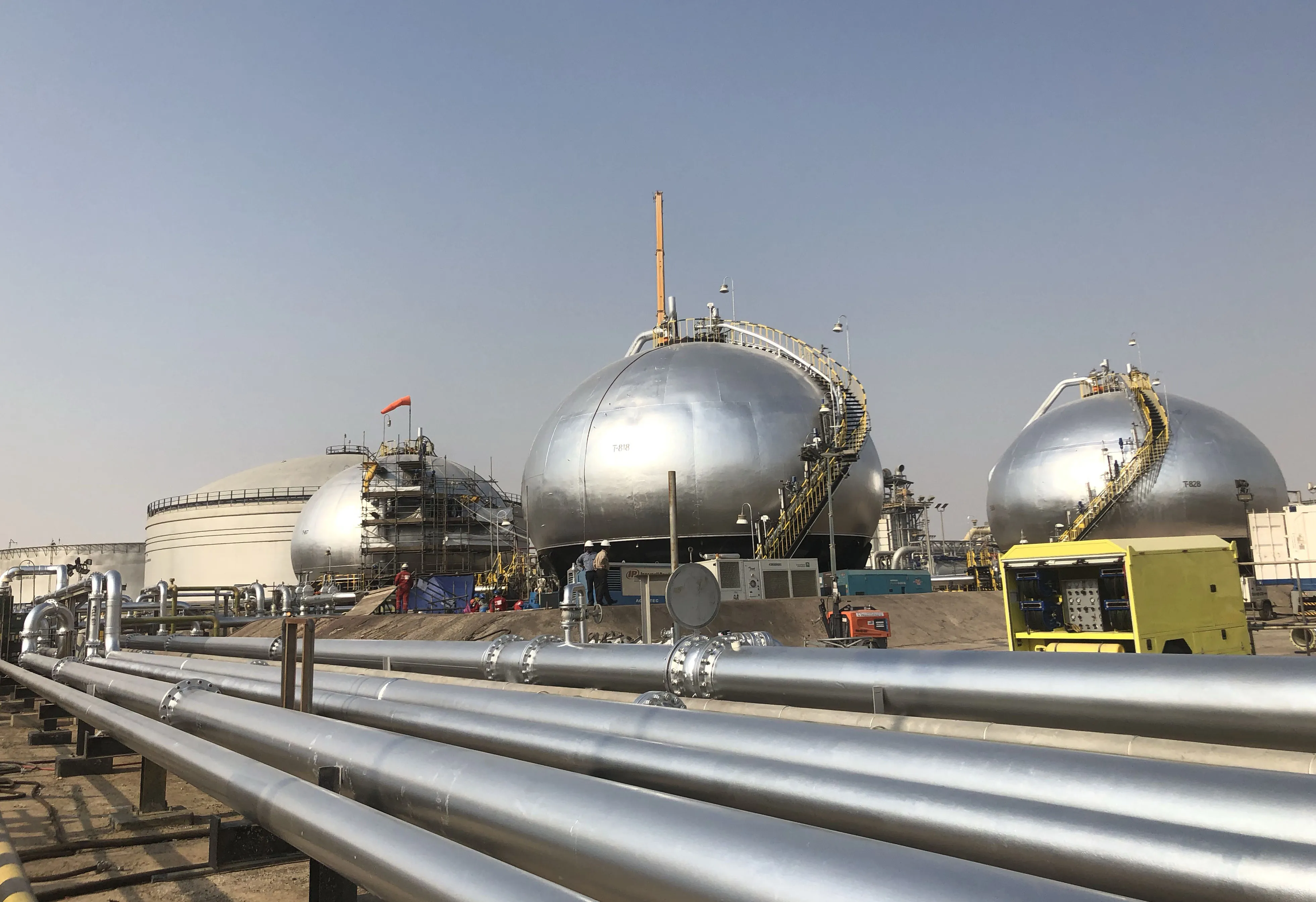 Three-phase spheroids stand behind pipelines at Saudi Aramco's crude oil processing facility in Abqaiq, Saudi Arabia.