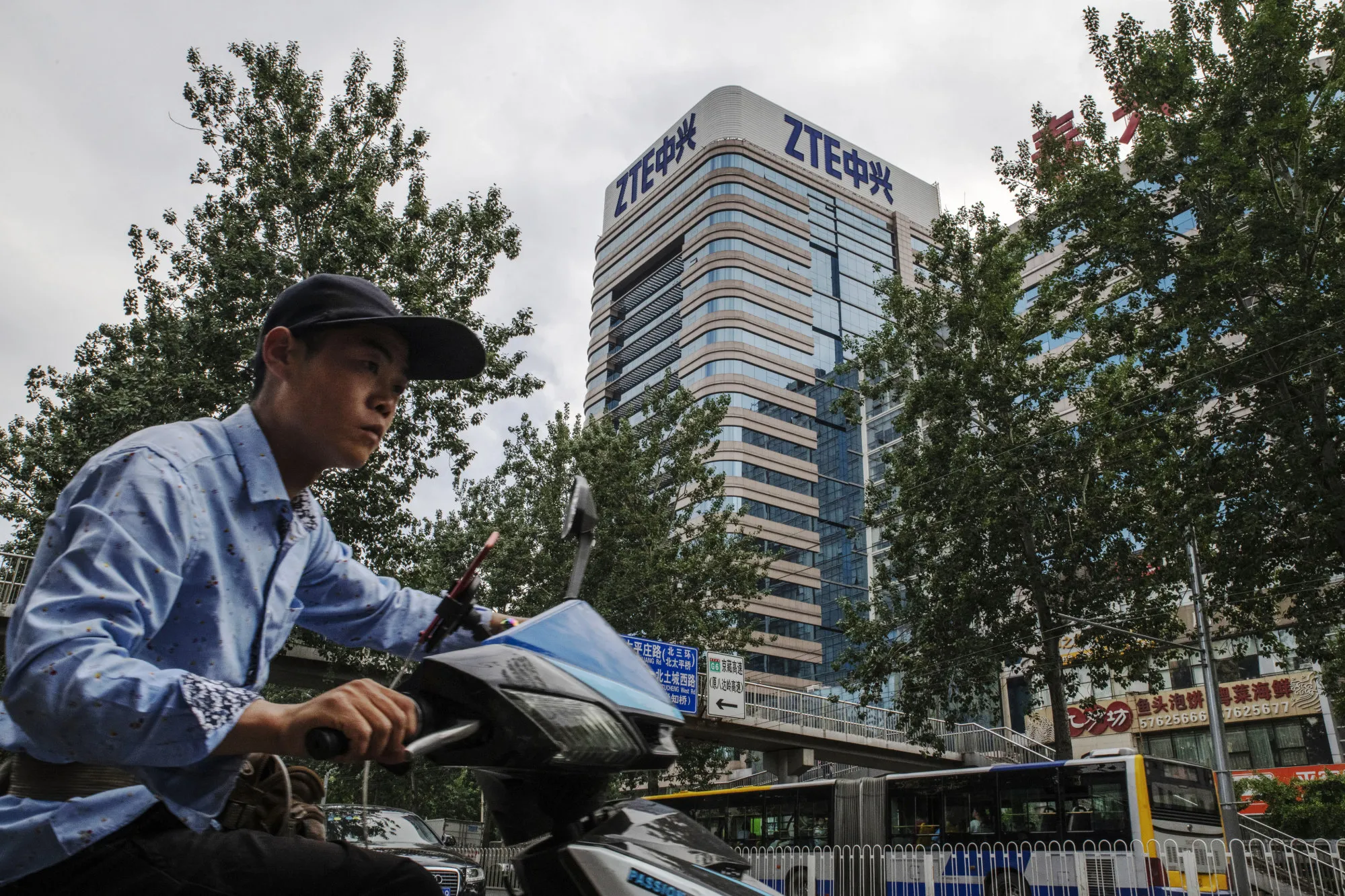 A man rides a motorcycle past a ZTE Corp. building in Beijing, China.