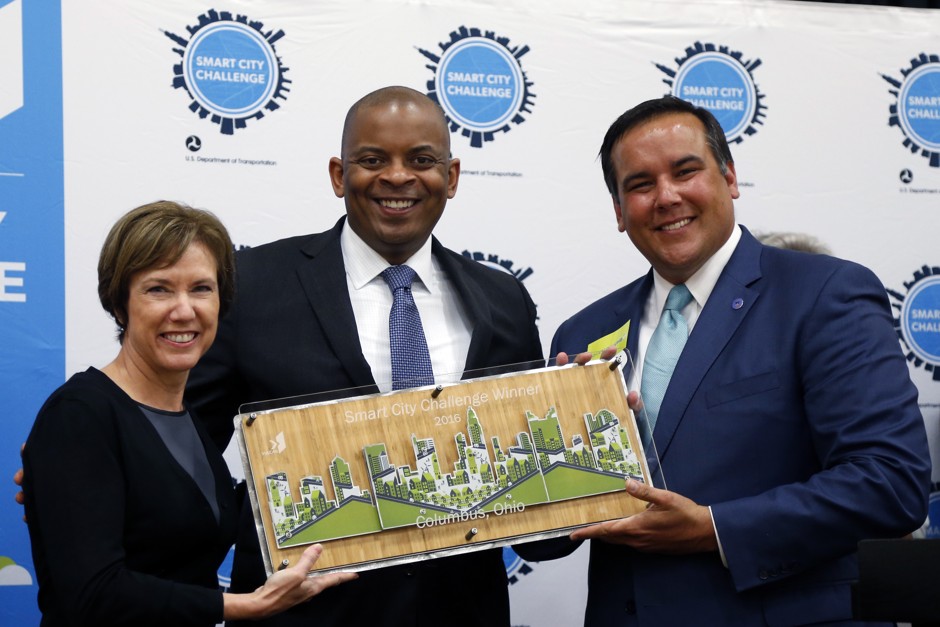 Barb Bennett, left, president/COO of Vulcan Inc, and former U.S. Transportation Secretary Anthony Foxx, center, present the Smart City Challenge award to Columbus Mayor Andrew Ginther in 2016.